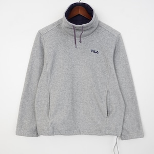 Pu&ograve; includere: Un pullover in pile grigio con collo alto foderato blu navy e coulisse. Il logo Fila &egrave; ricamato sul petto. Il pullover ha due tasche laterali ed &egrave; appeso a una gruccia di legno.