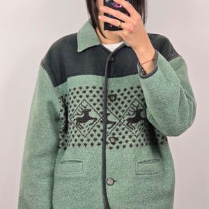 May include: A green and black wool jacket with a deer pattern. The jacket features a collared neckline, two front pockets, and three buttons. The deer pattern is in a diamond shape.