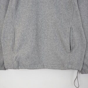 Pu&ograve; includere: Primo piano di una giacca in pile grigia. La giacca ha due tasche laterali e un cordino sull'orlo inferiore. Il tessuto &egrave; un materiale morbido e strutturato. La giacca &egrave; di colore neutro, adatta a vari outfit.