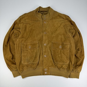 Può includere: Un giubbotto bomber in camoscio color marrone chiaro con colletto alla coreana, chiusura frontale con bottoni e due ampie tasche applicate con patta abbottonata sul petto. La giacca presenta polsini e orlo a coste per una vestibilità definita.
