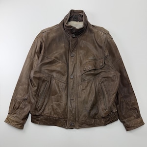 Könnte beinhalten: Eine braune Lederjacke mit Stehkragen und Knopfverschlüssen, einer Knopfleiste vorne, zwei vertikalen Reißverschlusstaschen an der Taille und einer Brusttasche mit Knopfklappe. Der Saum und die Ärmelbündchen sind mit Rippstrick versehen.