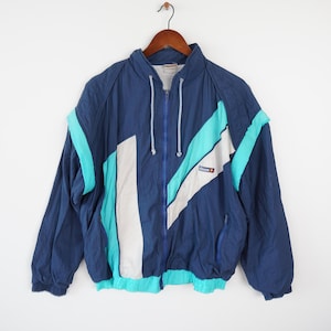 May include: A blue, white, and turquoise color-blocked windbreaker jacket with a zipper closure and the word "ellesse" on the right side.