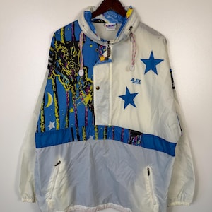 May include: A vintage white, blue, and gray anorak jacket with a hood. The jacket features a colorful design on the upper portion with stars and a night sky theme. It has a half-zip closure, two front pockets, and the text "ALEX" on the front.