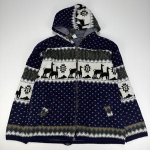 Peut inclure: Une veste à capuche zippée bleu marine, blanche et grise présentant un motif répétitif de lamas et de soleils géométriques. Ce vêtement en tricot comprend une fermeture éclair intégrale, deux poches avant et une capuche assortie au motif.