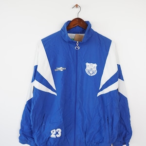 May include: A blue and white vintage Diadora track jacket with a white logo and a white crest with the text "Hull City" on the front. The jacket has a white number "23" on the left side of the chest.