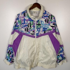 May include: A vintage white and purple zip-up jacket with a high collar. The jacket features a geometric pattern in blue, green, and black on the upper portion and sleeves. The lower portion is white with purple accents and two front pockets.