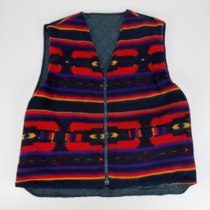 May include: A sleeveless vest featuring a fuzzy fleece exterior with a vibrant horizontal pattern in red, navy blue, purple, and yellow. The garment has a full-length front zipper closure and a dark navy blue quilted lining visible at the collar.