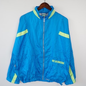 Könnte beinhalten: Eine blaue Nylonjacke mit neongrünen Akzenten und dem Schriftzug "NIKE INTERNATIONAL" auf der Vorderseite.