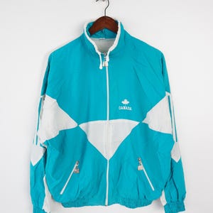 May include: A turquoise blue and white windbreaker jacket with a zipper closure and a white logo that says "CANADA" with a maple leaf.