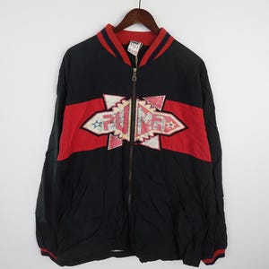 May include: A black zip-up jacket with red and white accents. The jacket features a large "PUMA" logo with a geometric design.