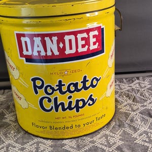 May include: A vintage yellow metal Dan-Dee potato chip tin with a lid and handle. The front features the red and white Dan-Dee logo, the text Potato Chips, and the phrase Flavor Blended to your Taste. The tin is marked with a net weight of 1 1/2 pounds.