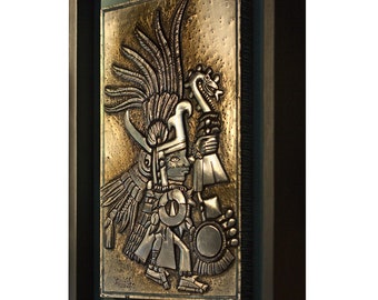 May include: A framed metal relief sculpture depicting an Aztec warrior in profile. The artwork features intricate details, including a feathered headdress, ceremonial objects, and a textured background. The frame is black, and the artwork is set against a green background.