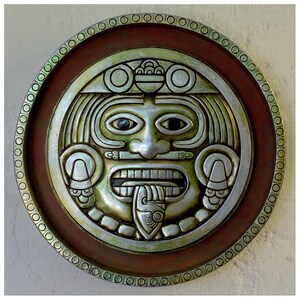 May include: A silver and green circular wall decor with a stylized face, surrounded by a brown wooden frame with a decorative border.