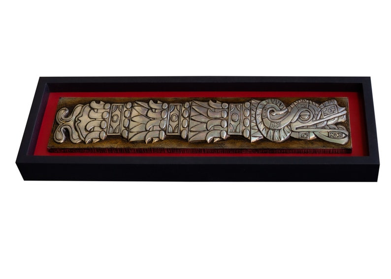 May include: A silver-colored metal relief sculpture of a stylized serpent or dragon with intricate details, framed in black with a red mat.