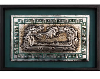 May include: A framed metal relief sculpture featuring a stylized serpent with intricate details. The artwork is silver-toned with a green border and a dark frame. The serpent is depicted with an open mouth and flowing elements.