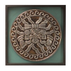 Puede incluir: Una pieza de arte de pared circular de plata y oro con una cara estilizada en el centro. La cara tiene una nariz grande, ojos grandes y una boca ancha. La pieza está enmarcada en un marco negro con un passe-partout verde.