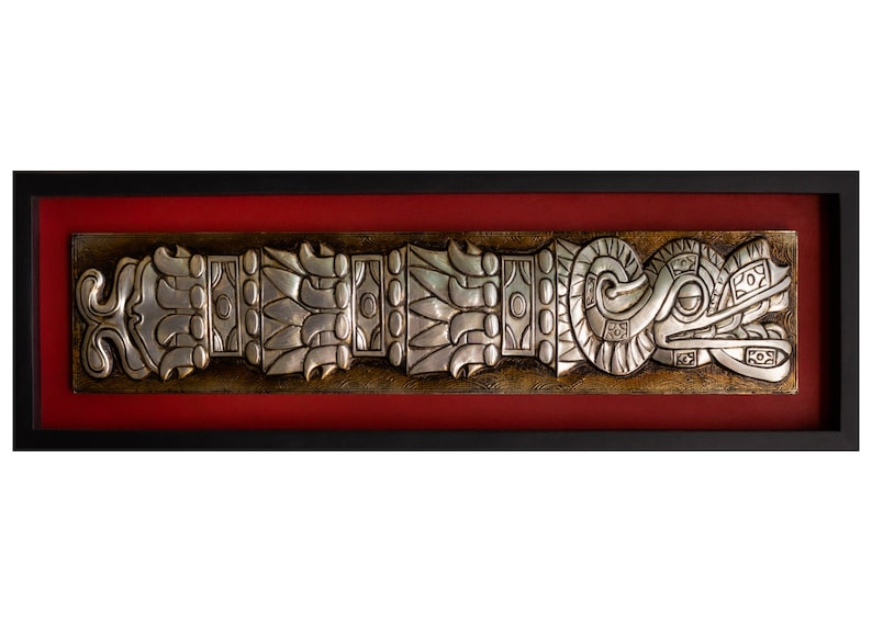 May include: A silver framed artwork depicting a stylized, detailed, silver relief of a serpent with a feathered headdress. The artwork is framed in a black frame with a red mat.