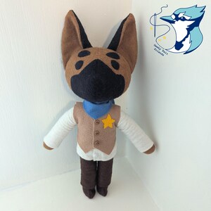 May include: A plush animal doll with brown and black fur, wearing a tan vest with three buttons and a yellow star patch, a blue neckerchief, white long sleeves, and dark brown trousers. A logo with a blue bird and the text Geeky Felt Friends.