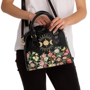 May include: Black leather handbag with a floral print and a gold sun and moon design. The bag has a top handle and a shoulder strap.