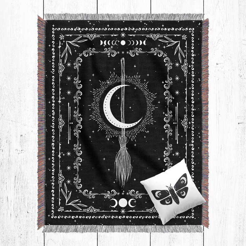 K&ouml;nnte beinhalten: Schwarz-wei&szlig;e gewebte Wurfdecke mit einem Mond- und Besen-Design. Die Decke hat einen Fransenrand und ein wei&szlig;es Kissen mit einem schwarzen Schmetterlingsdesign.