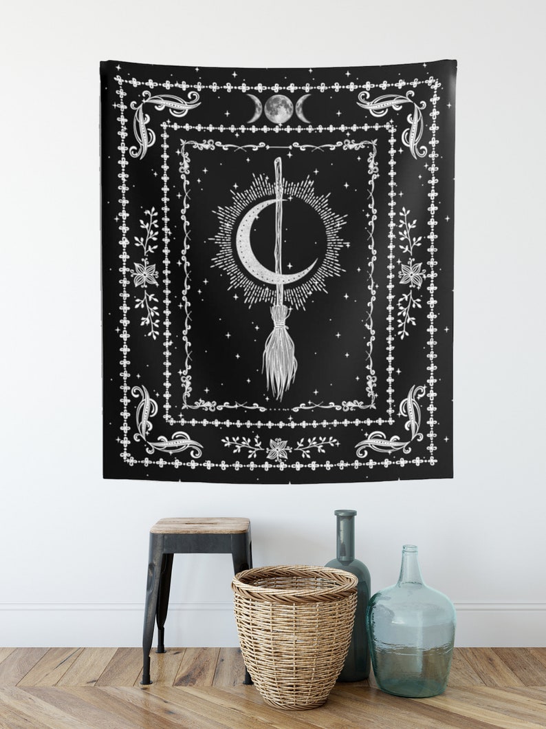 May include: Black and white tapestry with a crescent moon and a broom with stars in the background. The tapestry has a decorative border with floral and geometric designs.