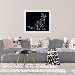 May include: A gray sofa with a black and white geometric throw blanket and three pillows. The pillows are pink, black and white, and gray with a black and white watercolor design. A black and white geometric illustration of a dog is hanging on the wall above the sofa.