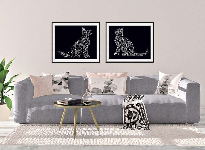 May include: Two black and white geometric animal illustrations in frames, a dog and a cat, hanging above a gray couch with pillows and a throw blanket.