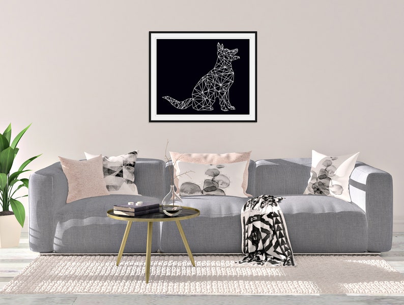 May include: A gray couch with pillows and a throw blanket in front of a white wall with a framed black and white geometric dog illustration.