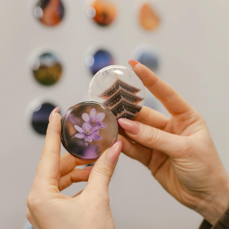 A person's hands holding a small, round magnet with a purple flower design.