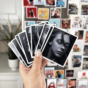 A hand holding a fan of black and white photographs of a woman's face, with a collage of various other photographs visible in the background.