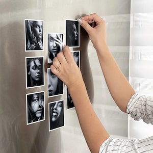 A person's hands are shown placing small black and white photographs onto a refrigerator door.