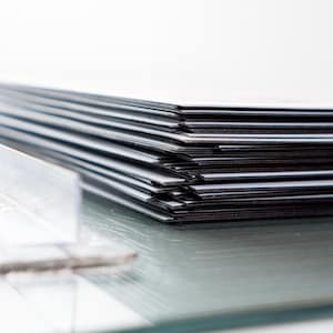 May include: A stack of rectangular, black and white cards or papers, possibly photographs or prints, arranged in a neat pile. The edges of the cards are visible, creating a striped effect. The surface is reflective, with a blurred object in the foreground.