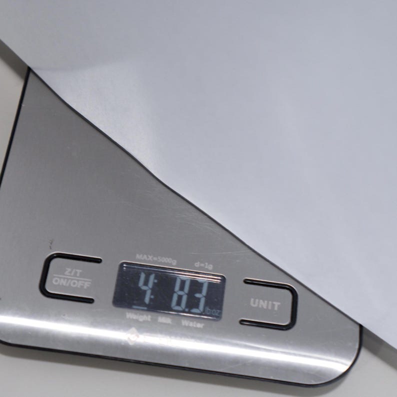 May include: A digital kitchen scale with a silver finish displays a weight of 48.3 ounces. The scale has an on/off button and a unit button. The maximum weight capacity is 3000 grams. The scale is partially covered by a white sheet of paper.