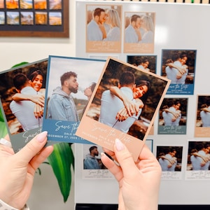 A person's hands holding two small wedding invitation cards with photographs of a couple embracing.