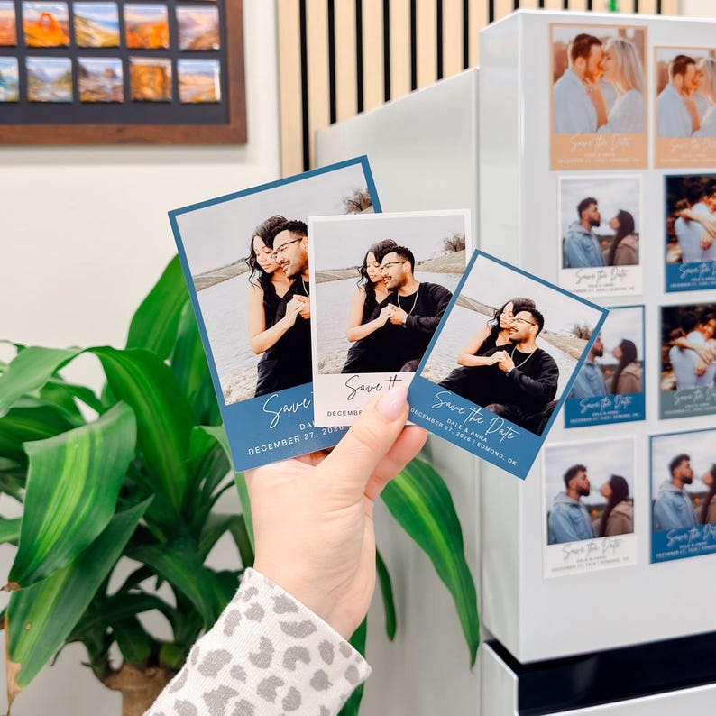 A hand holding three small blue and white wedding invitation cards with a couple posing together.