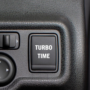 Könnte beinhalten: Ein schwarzer Knopf mit der Aufschrift "TURBO TIME" in weißer Schrift.