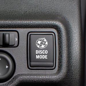 May include: A black button with a white disco ball icon and the text "DISCO MODE" on a car dashboard.