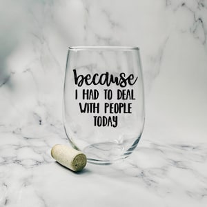 May include: A clear stemless wine glass with black text that reads "because I HAD TO DEAL WITH PEOPLE TODAY". A cork rests near the glass. The background is a white and gray marble pattern.
