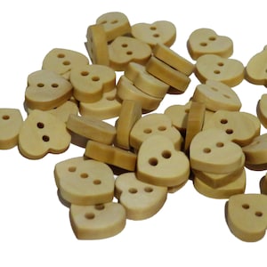 Può includere: Un mucchio di bottoni di legno a forma di cuore di colore marrone chiaro con due fori ciascuno.