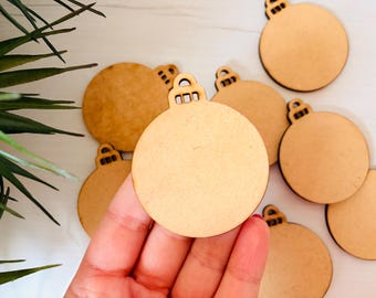 May include: A collection of unfinished wooden Christmas ornament cutouts. Each ornament is a circle with a small loop at the top for hanging. The ornaments are a light brown color and are ready for painting or decorating.