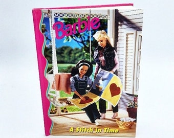 May include: A Barbie book titled "A Stitch in Time" with a pink cover. The cover art features two Barbie dolls, one on a swing and the other standing, with a quilt. The Barbie logo is in pink and blue.