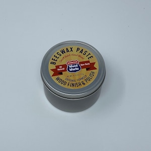 May include: A silver tin of Interstate Wood Works Beeswax Paste. The label is yellow with red and black lettering. It says "Small Batch, Hand Mixed", "All Natural", "Non-Toxic", "Original Formula", "Wood Finish & Polish", and "Net Wt. 6.25 oz / 177g".