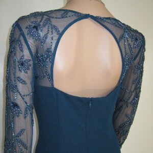 May include: Teal formal dress with a keyhole back and long sleeves. The sheer sleeves have intricate beaded floral patterns. The dress has a fitted bodice and a subtle, elegant design.