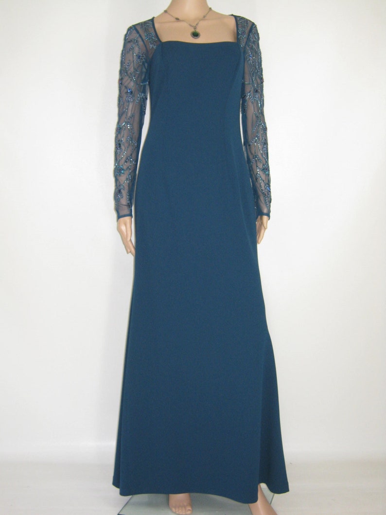 May include: A teal evening gown with a square neckline and long, sheer sleeves adorned with blue beading. The dress features a floor-length skirt and is shown on a mannequin.