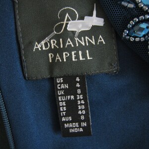 May include: A teal dress label with the brand name "ADRIANNA PAPELL" in white. The label shows size conversions for US, CAN, UK, EU/FR, DE, ES, IT, and AUS. The dress is made in India.