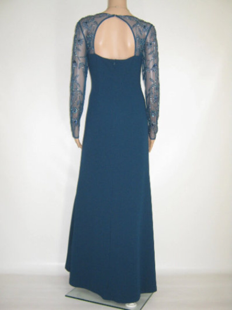 May include: A teal evening gown with long sleeves and a keyhole back. The sheer sleeves are embellished with detailed beadwork. The dress features a fitted bodice and a flowing skirt, ideal for formal events.