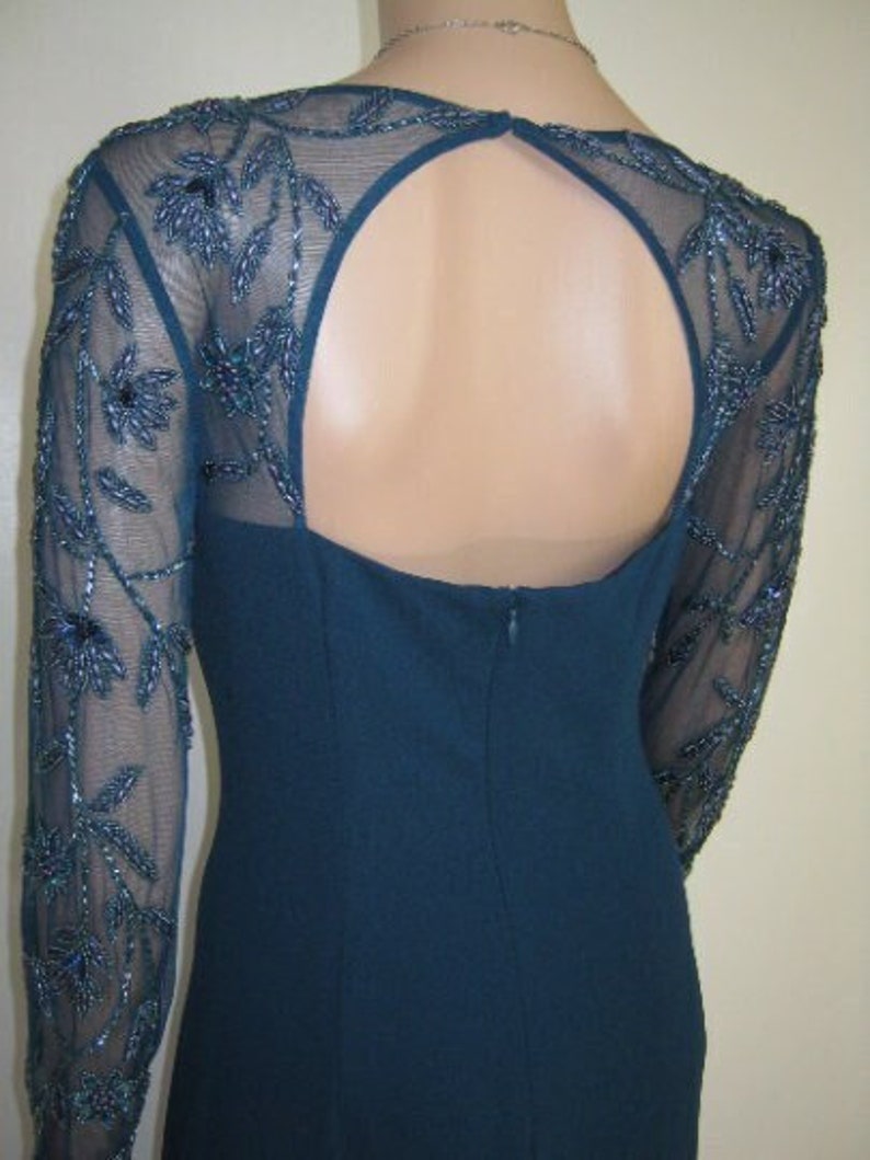 May include: Teal formal dress with a keyhole back and long sleeves. The sheer sleeves have intricate beaded floral patterns. The dress has a fitted bodice and a subtle, elegant design.
