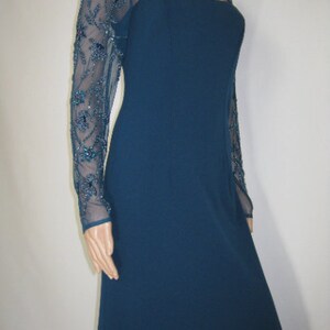 May include: A teal evening gown with sheer, long sleeves embellished with teal and blue beadwork. The dress has a square neckline and a fitted bodice that extends into a floor-length skirt. The dress is a classic design.