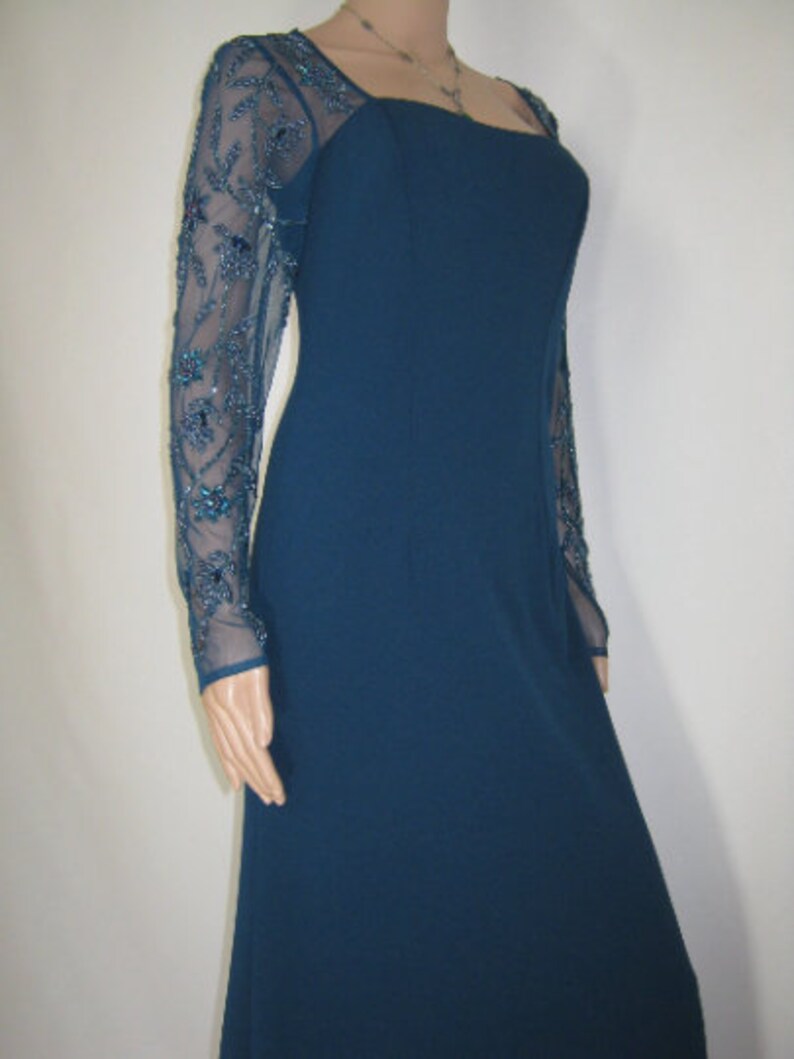 May include: A teal evening gown with sheer, long sleeves embellished with teal and blue beadwork. The dress has a square neckline and a fitted bodice that extends into a floor-length skirt. The dress is a classic design.