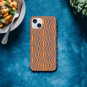 Op de afbeelding: Een smartphonehoesje met een golvend patroon in oranje en blauw. De hoes heeft een camera-uitsparing en ligt op een blauwe achtergrond. Het ontwerp is opvallend en modern, en biedt bescherming en een modieuze uitstraling voor de telefoon.